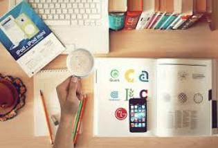 Étudiants en Génie Biologique : Travaillez depuis chez vous! Image représentant plusieurs livres fermés et ouverts, sur un bureau sur lequel il y a également des crayons et un ordinateur ouvert. Quelqu'un tient une tasse dans sa main.